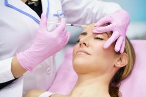 Aesthetic doctor injecting botox into the forehead of her middle-aged patient. photo