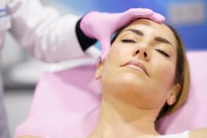 Doctor painting the area of a woman's face where the PDO suture treatment threads will be injected. photo