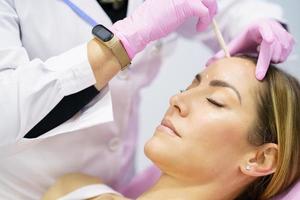 médico estético pintando en el rostro de su paciente las zonas a tratar con botox. foto