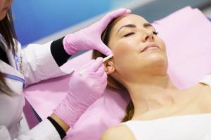 Doctor painting the area of a woman's face where the PDO suture treatment threads will be injected. photo