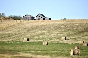 old farm on a hill with round bales in the foreground photo