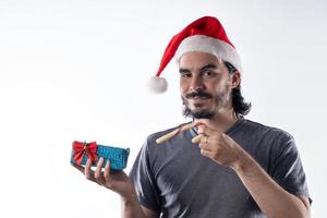 Medium shot portrait of smiling Latino man with red Santa Claus hat looking at camera holding Christmas presents , isolated on white background. Positive emotions, facial expressions photo