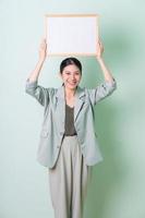 Young Asian businesswoman holding white board on green background photo