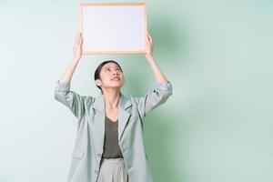Young Asian businesswoman holding white board on green background photo