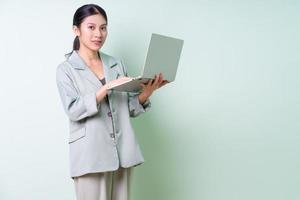Young Asian businesswoman holding laptop on green background photo