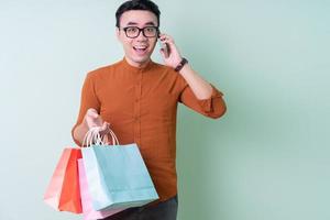 Young Asian man holding shopping bag on green background photo