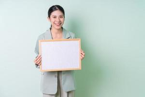 Young Asian businesswoman holding white board on green background photo