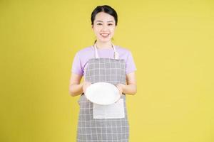 Young Asian housewife posing on yellow background photo