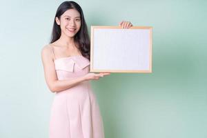 Hermosa joven asiática sosteniendo una pizarra blanca sobre fondo verde foto