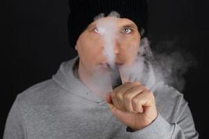 Unrecognizable man in the cloud of vape smoke. Guy smoking e-cigarette to quit tobacco. Vapor and alternative nicotine free smoking concept, copy space selective focus photo