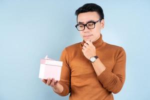 Asian man holding pink giftbox on blue background photo