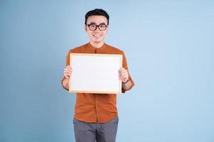 Young Asian man holding white board on blue background