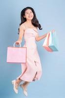 Beautiful young Asian woman holding shopping bag on blue background photo