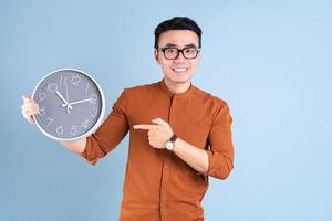 Young Asian man holding clock on blue background photo