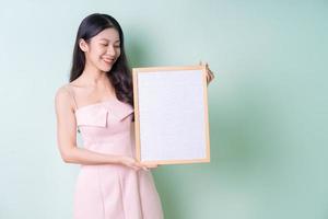 Beautiful young Asian woman holding white board on green background photo