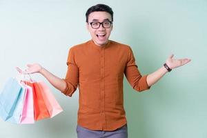 Young Asian man holding shopping bag on green background photo