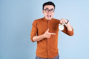 Young Asian man holding clock on blue background photo
