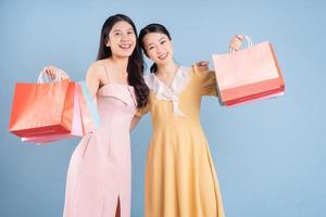 Dos jóvenes mujeres asiáticas sosteniendo una bolsa de compras sobre fondo azul. foto