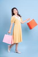 Beautiful young Asian woman holding shopping bag on blue background photo