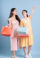 Two young Asian women holding shopping bag on blue background