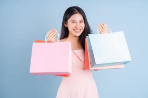 Hermosa joven asiática sosteniendo una bolsa de compras sobre fondo azul. foto