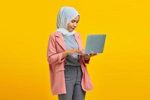 Retrato de hermosa joven estudiante universitaria con portátil sonriendo vistiendo chaqueta rosa aislado sobre fondo azul. foto