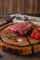 Raw cap rump beef - brazilian picanha on a wood cutting board with rosemary branch, tomatoes and spices. photo