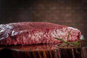 Raw marble denver beef on a wood resined cutting board with rosemary branch and bricks wall background - Closeup. photo