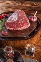 Raw cap rump beef - brazilian picanha - on a wood resined cutting board with spices. Wooden table. photo
