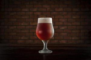 Isolated sweaty tulipa glass of refreshing amber ale draft beer with brick wall background. photo