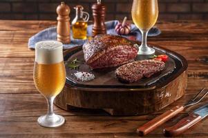 Two sweaty cold tulipa glasses of beer with grilled sliced cap rump steak on wooden cutting board  - brazilian picanha. photo