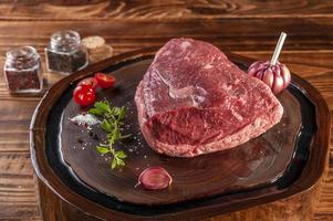 Raw cap rump beef - brazilian picanha - on a wood resined cutting board with spices. Wooden table. photo