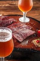 Grilled denver steak sliced on wooden cutting board with parrilla salt and two sweaty clod glasses of beer. Marble meat beef - Closeup. photo