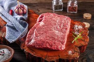 Raw marble denver beef on a wood resined cutting board with spices and rosemary branch. photo