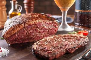 Grilled sliced cap rump steak with two glasses of beer on wooden cutting board. Marble meat beef - Brazilian picanha.