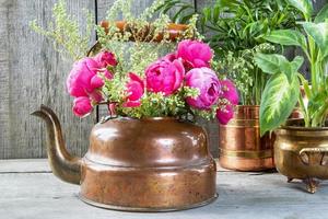 Rosas rosadas en hervidor de latón de cobre antiguo y plantas verdes