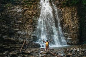 Traveler man with a yellow backpack standing on background of a waterfall. Travel lifestyle concept. photo