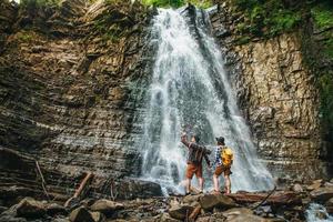 Man and woman hikers trekking a rocky path against the background of a waterfall and rocks photo