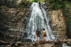 Man and woman hikers trekking a rocky path against background of a waterfall and rocks photo