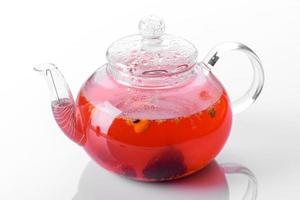 Delicious tea of berries and fruits in a beautiful glass teapot on a white background with reflection photo