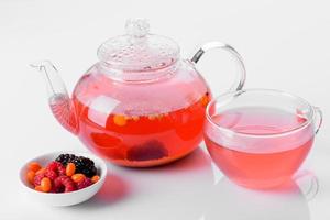 Delicious tea of berries and fruits in a beautiful glass teapot on a white background with reflection photo