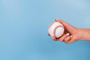 Female hand with white nails holding white baseball on blue background photo