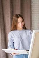 Joven artista femenina reflexiva pintando sobre el lienzo en el estudio sosteniendo una paleta con acuarelas foto