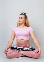 Hermosa joven mujer caucásica sentada en posición de yoga y meditando aislado sobre fondo gris foto