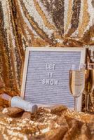 Felt letter board Let It Snow on golden shiny background with champagne glasses and bottle photo