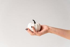 Female hand with black nails holding white and black halloween pumpkin photo