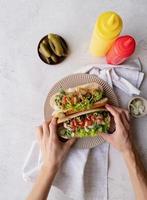 Hot dog with sausage, letuce, cucumber and onion on beige plate on concrete background