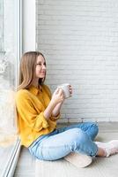 Atractiva mujer adolescente en camisa amarilla bebiendo té sentados en el suelo foto