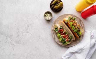 Hot dog with sausage, letuce, cucumber and onion on beige plate on concrete background