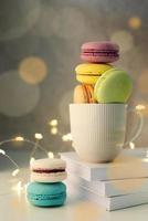 white coffee cup filled with macaroons on the table, fairy lights and bokeh background photo